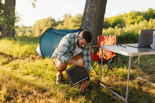 Camper setting up a portable solar charger on the grass next to a tent and outdoor workspace