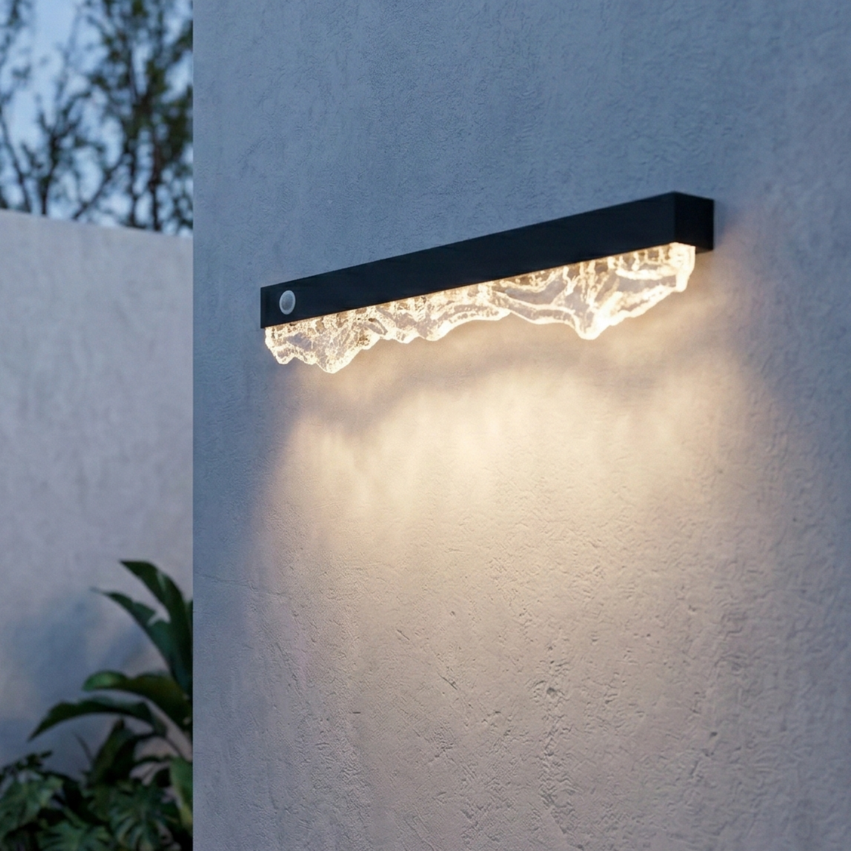 Modern outdoor wall light fixture on a textured white wall with a plant in the corner.
