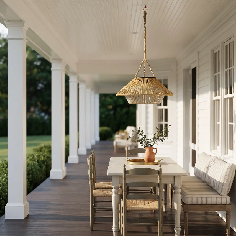 A woven wicker pendant light hangs over a dining table on a bright white porch with columns, chairs, and a cushioned bench.