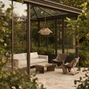 Inside a modern glass conservatory, the HAIKU PT0902 Rattan Duo Solar Ceiling Light hangs above a minimalist seating area. Its intricate woven design complements the sleek furniture, while the dual-layer shade diffuses light softly, turning the space into a tranquil retreat surrounded by greenery.