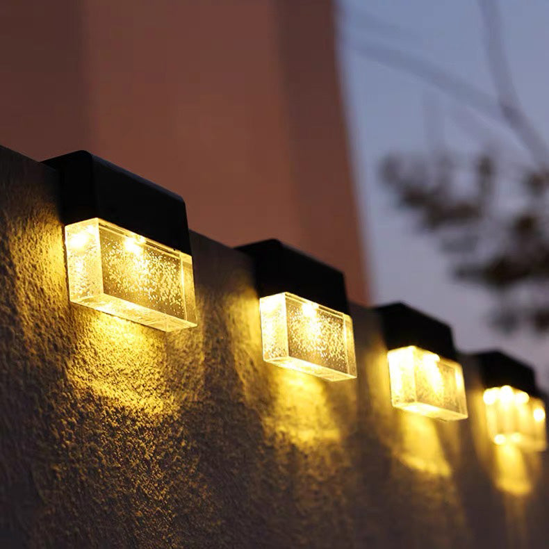 A row of outdoor solar wall lights mounted on a textured wall, casting a warm yellow glow in the evening.