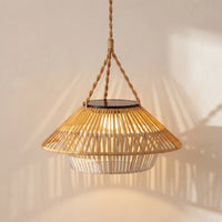 A natural bamboo and rattan pendant light with a woven shade, suspended by a thick rope from a solar panel, casting warm light on a textured beige wall.