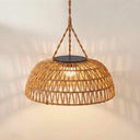 A woven natural rattan dome pendant light with a warm glowing light inside, suspended by a twisted rope chain against a textured off-white wall.