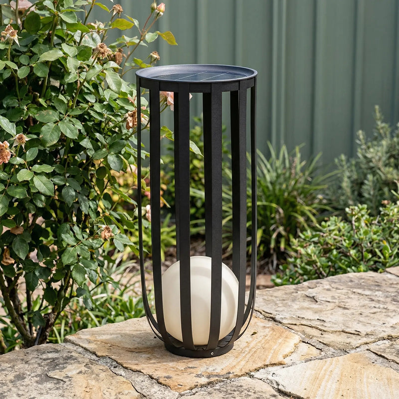 Black metal lantern with a white candle on a stone surface outdoors