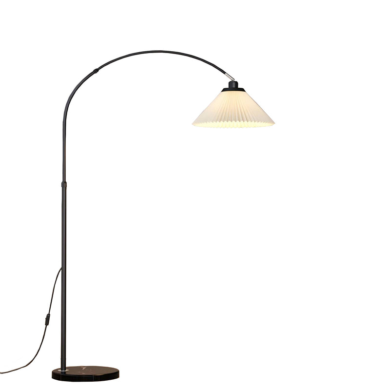 A modern floor lamp with a black arched metal stand, a round dark base, and a pleated white shade that glows warm white when lit, shown on a plain white background.