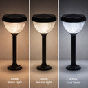 Three solar outdoor landscape lights shown side by side in warm, neutral, and cool white light modes, each with a black ribbed glass shade and base on a plain surface.