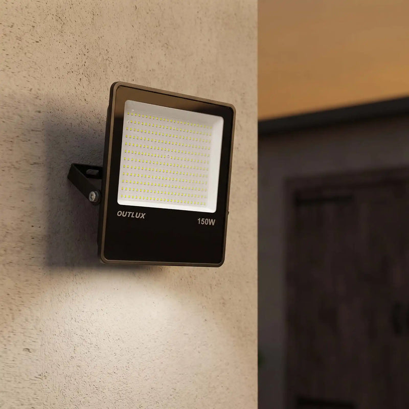 An OUTLUX 150W outdoor LED floodlight mounted on a textured beige wall, casting light downward, with a blurred interior doorway in the background.