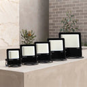 Four black outdoor LED floodlights of different wattages (30W, 50W, 70W, 150W) arranged in ascending size order on a concrete ledge, with a stone and brick wall background.