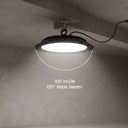 A high-bay LED warehouse light suspended from a ceiling, emitting a bright glow with a dotted arc overlay indicating a 120-degree wide beam. White text in the center reads '100 lm/W 120° Wide Beam'.