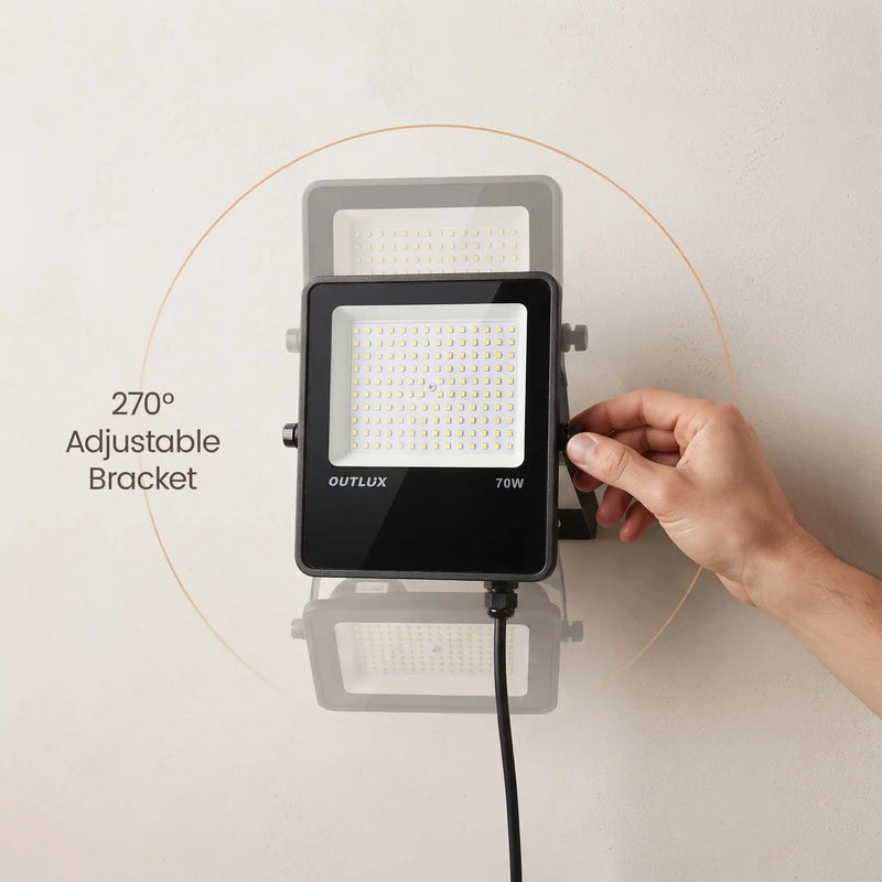 A wall-mounted OUTELUX 70W LED floodlight shown with a hand adjusting its side bracket, with text reading '270° Adjustable Bracket' on a plain beige wall.