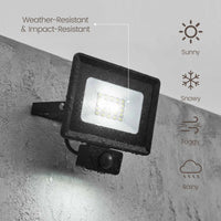 Black outdoor LED floodlight with a built-in motion sensor, mounted on a gray concrete wall. The image includes text and icons indicating weather resistance and suitability for sunny, snowy, foggy, and rainy conditions.