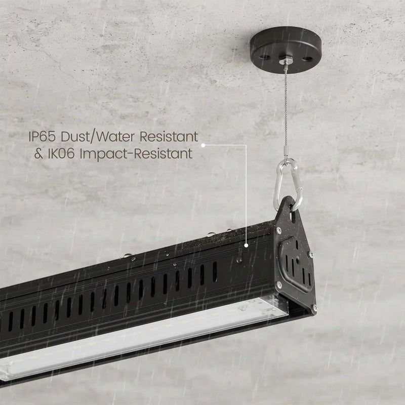 A black industrial ceiling-mounted light fixture shown hanging from a ceiling in a rain-swept environment, with overlaid text reading 'IP65 Dust/Water Resistant & IK06 Impact-Resistant.' This is not a clean product-only studio shot because the real environment and rain create a lifestyle-like presentation, so subject_type is Lifestyle rather than Product/Packaging or Instruction Diagram.