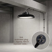 A black industrial-style pendant light hanging from a ceiling in a concrete warehouse or studio space. The light has a ribbed shade and an adjustable arm extending to the right.